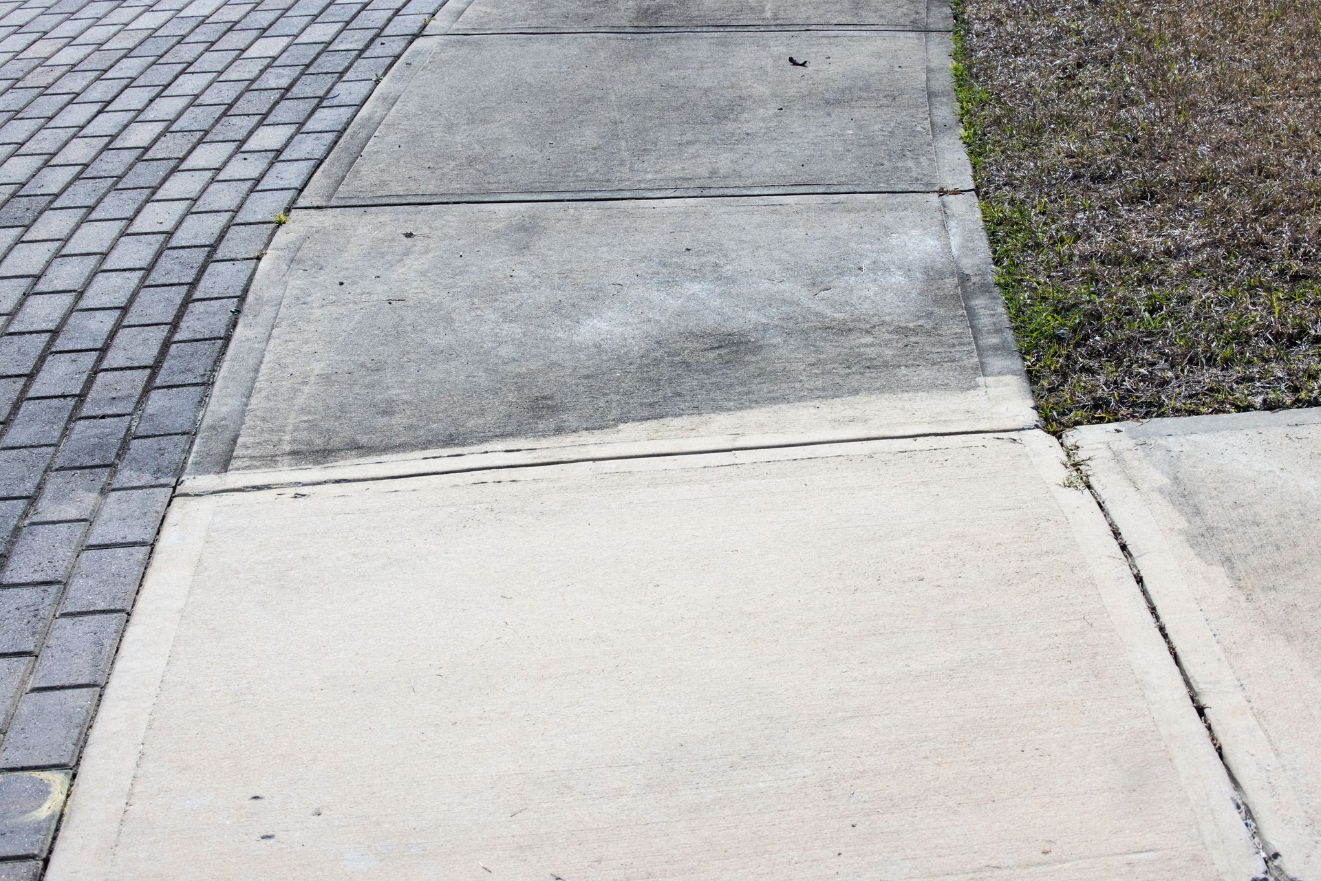 Patrially cleaned and partial irty cement sidewalk in front of a homeafter some of it has been pressure washed.